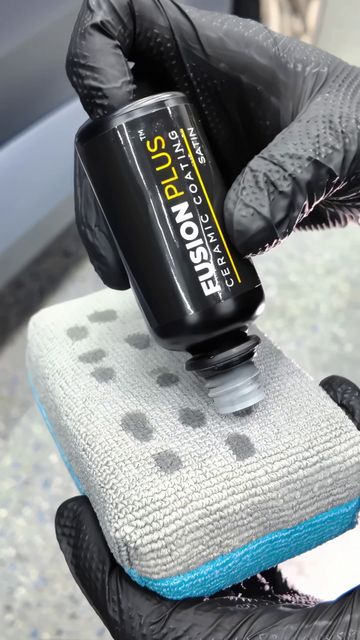 Gloved hands squeeze black Emulsion Plus bottle onto a gray microfiber cloth