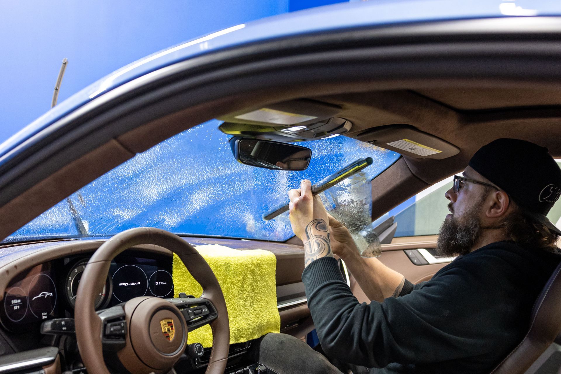 Driver inside a car holds up a smartphone while a blue tarp covers the windshield.