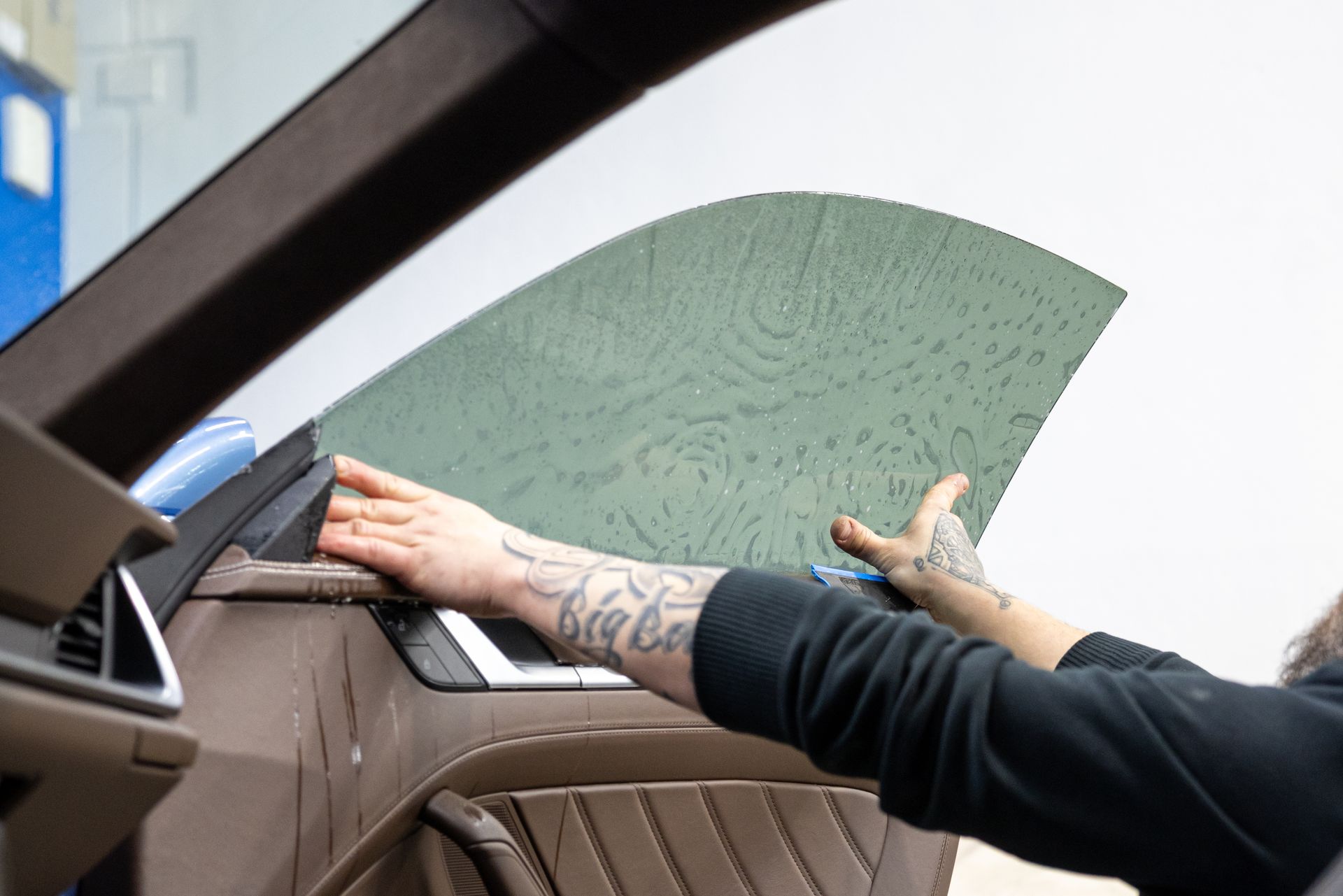 Person opening a car door with a green-tinted window panel on a brown interior