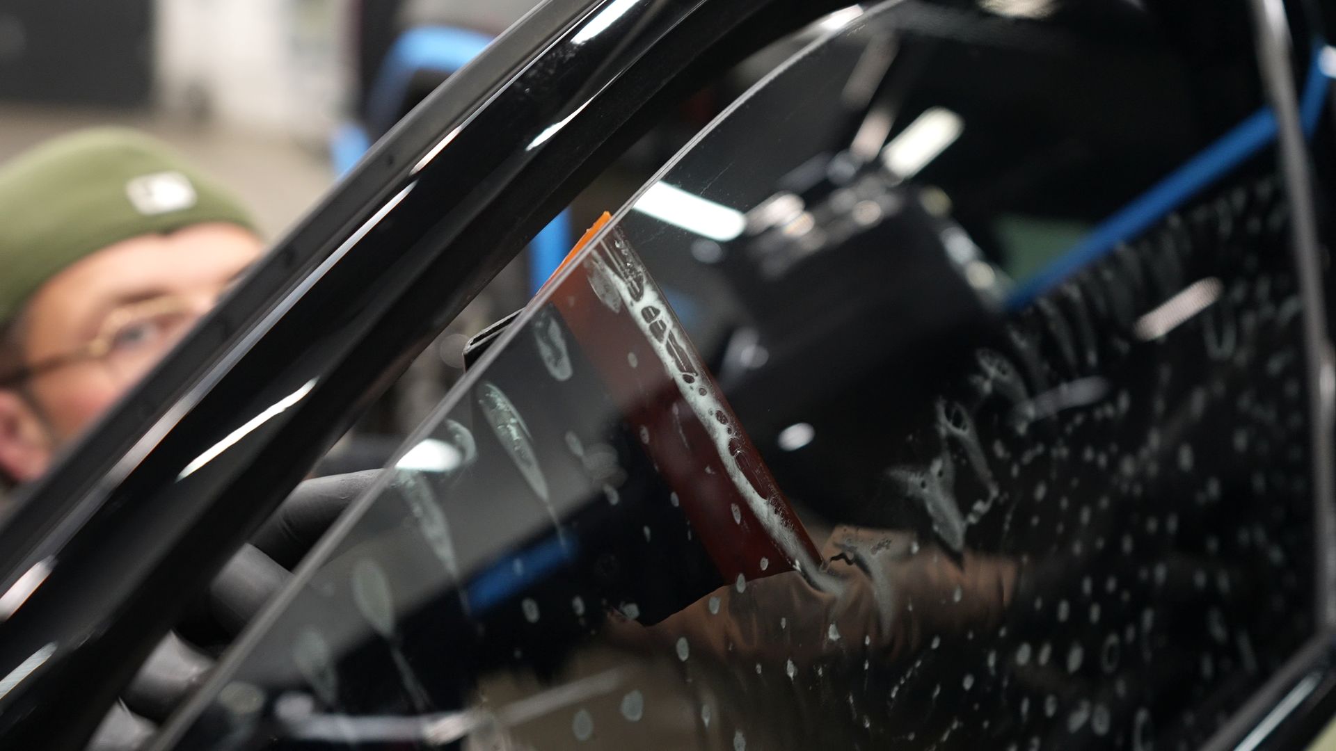 Person inspecting a black car window with raindrops, reflections visible in the glass