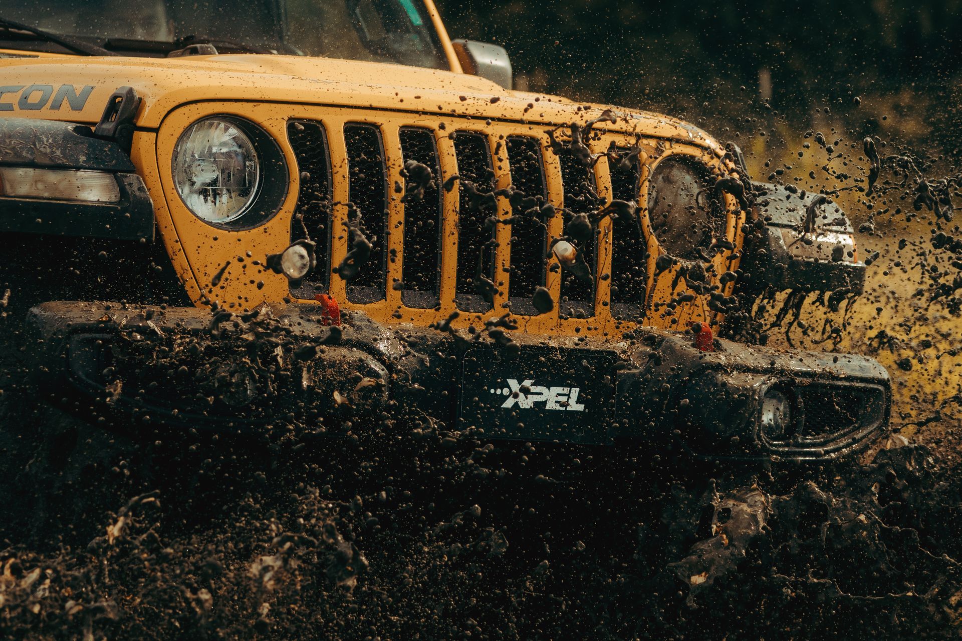 Yellow Jeep splashing through muddy water, front grille close-up in an off-road scene