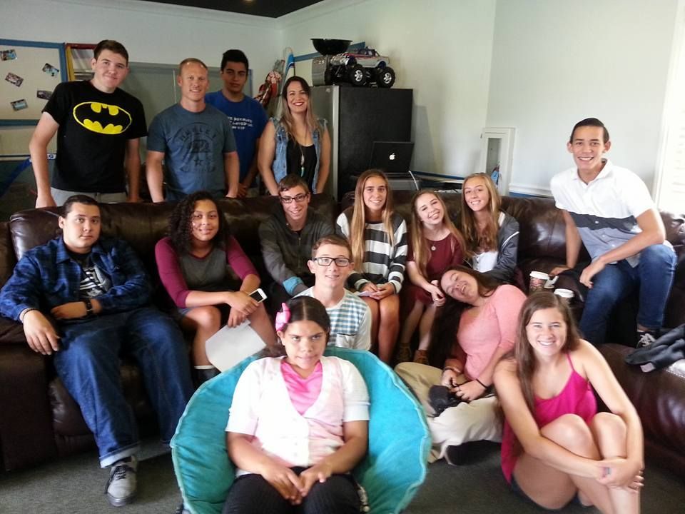 Group of teens and adults smiling on a brown leather couch in a room with a blue bean bag chair.