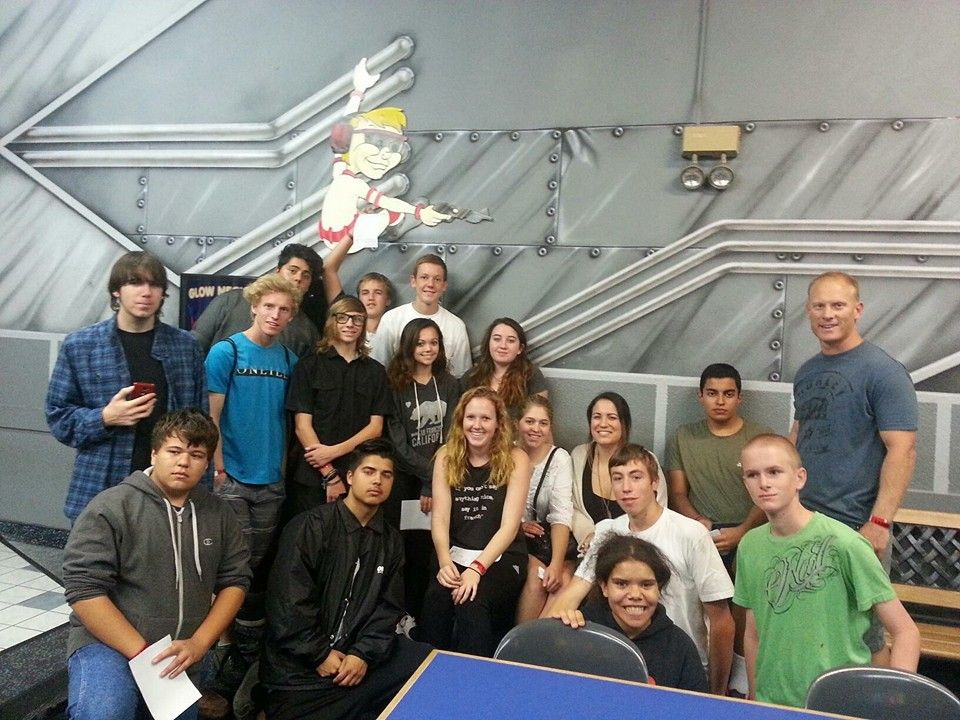 Group of students and adults posing in front of a painted wall with an industrial cartoon figure.
