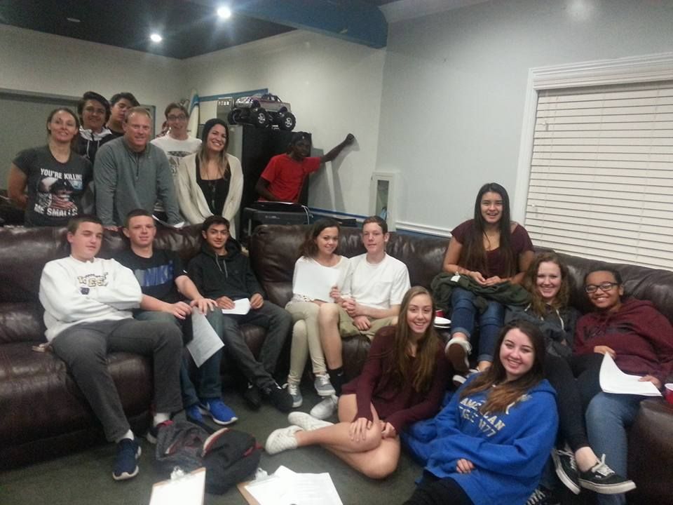 Group of students in a room; some are on a couch, others stand behind. They appear to be studying or socializing.