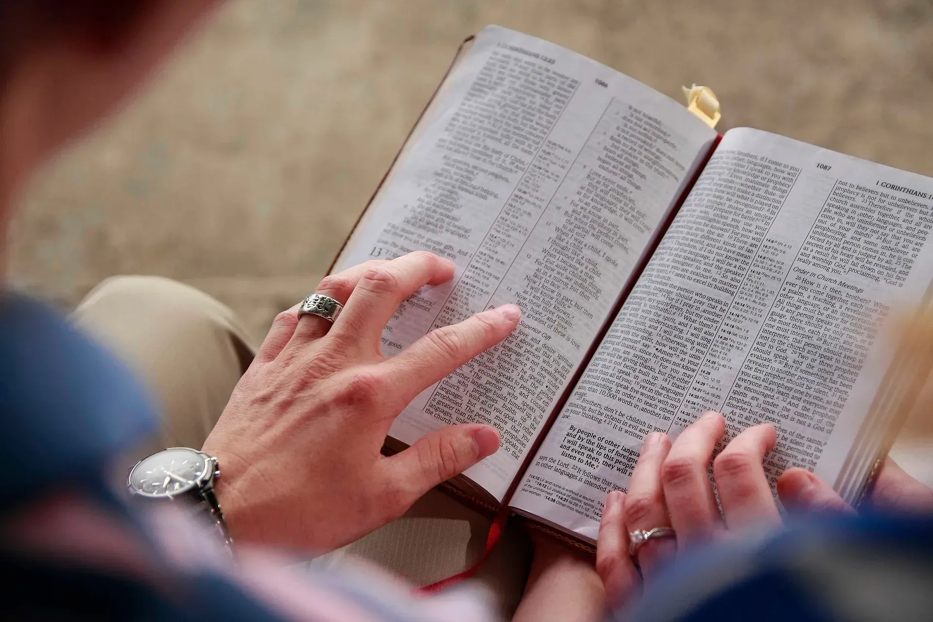 Two people reading an open Bible, hands pointing at the text.