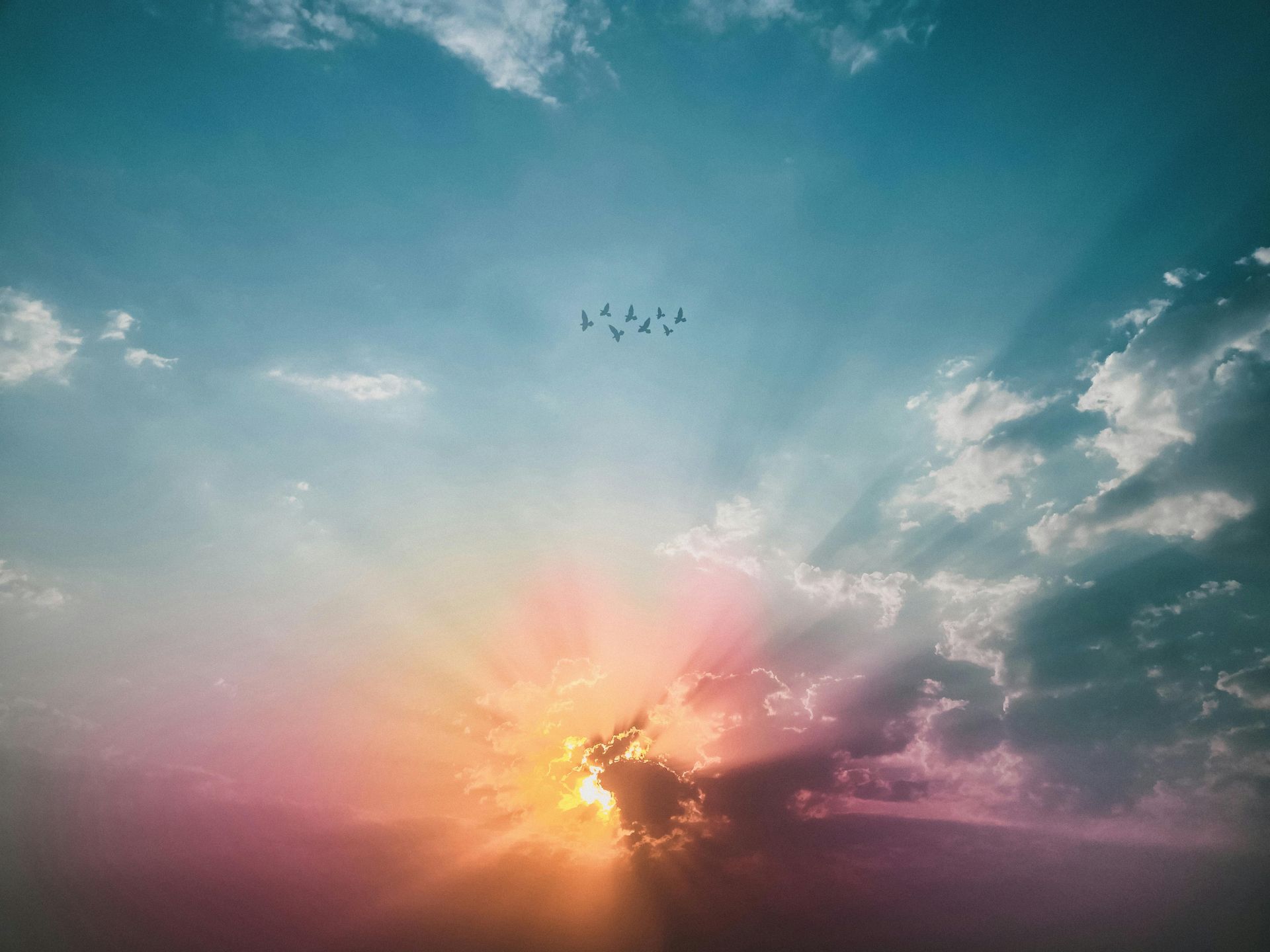 Sunset sky with birds in flight; rays of light burst through clouds, vibrant colors.