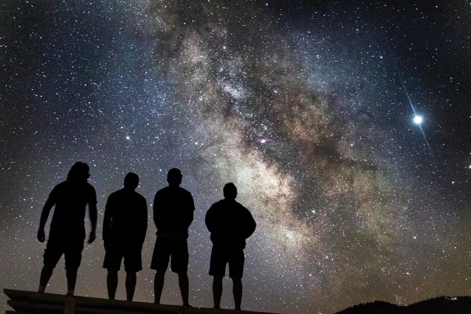 Silhouetted figures of four people gaze at the starry Milky Way galaxy.