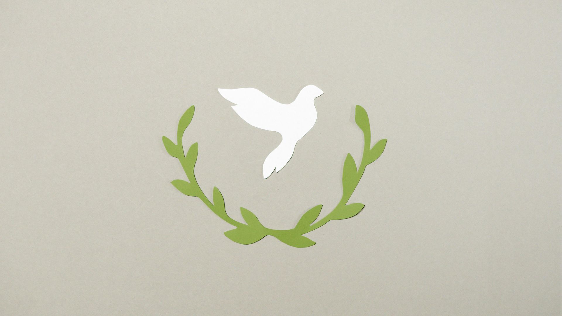 White dove within a green laurel wreath on a light-colored background.