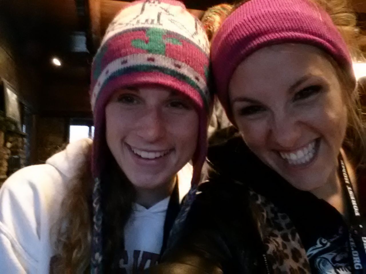 Two smiling women, wearing beanies, close-up selfie. One has a white hoodie, the other a leopard-print jacket.