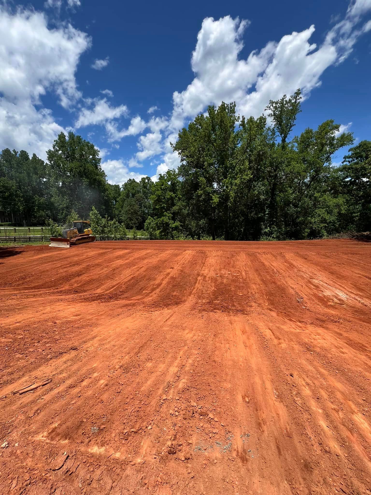 A large dirt field with trees in the background and a blue sky with clouds.