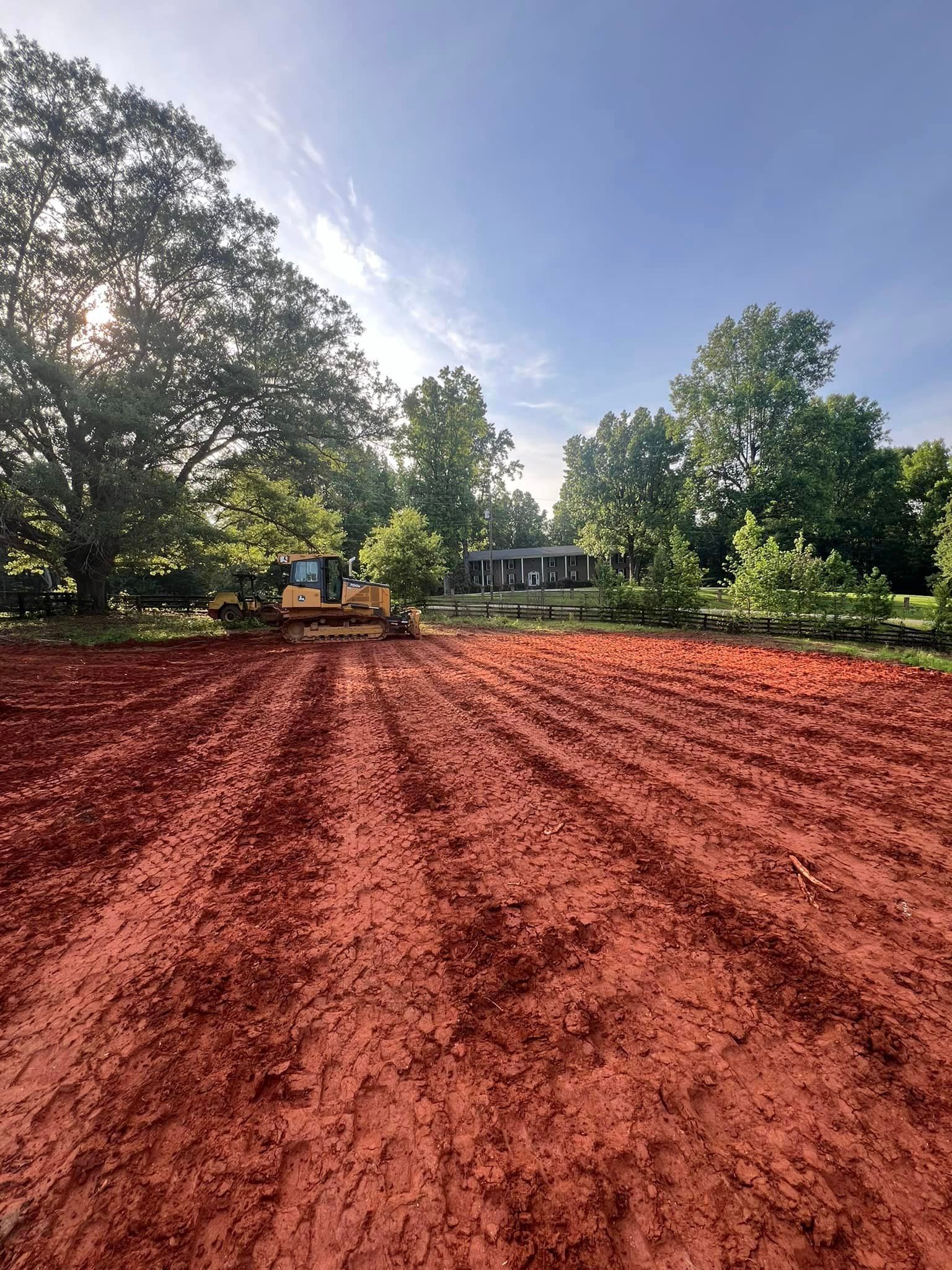 A bulldozer is moving dirt in a field with trees in the background.