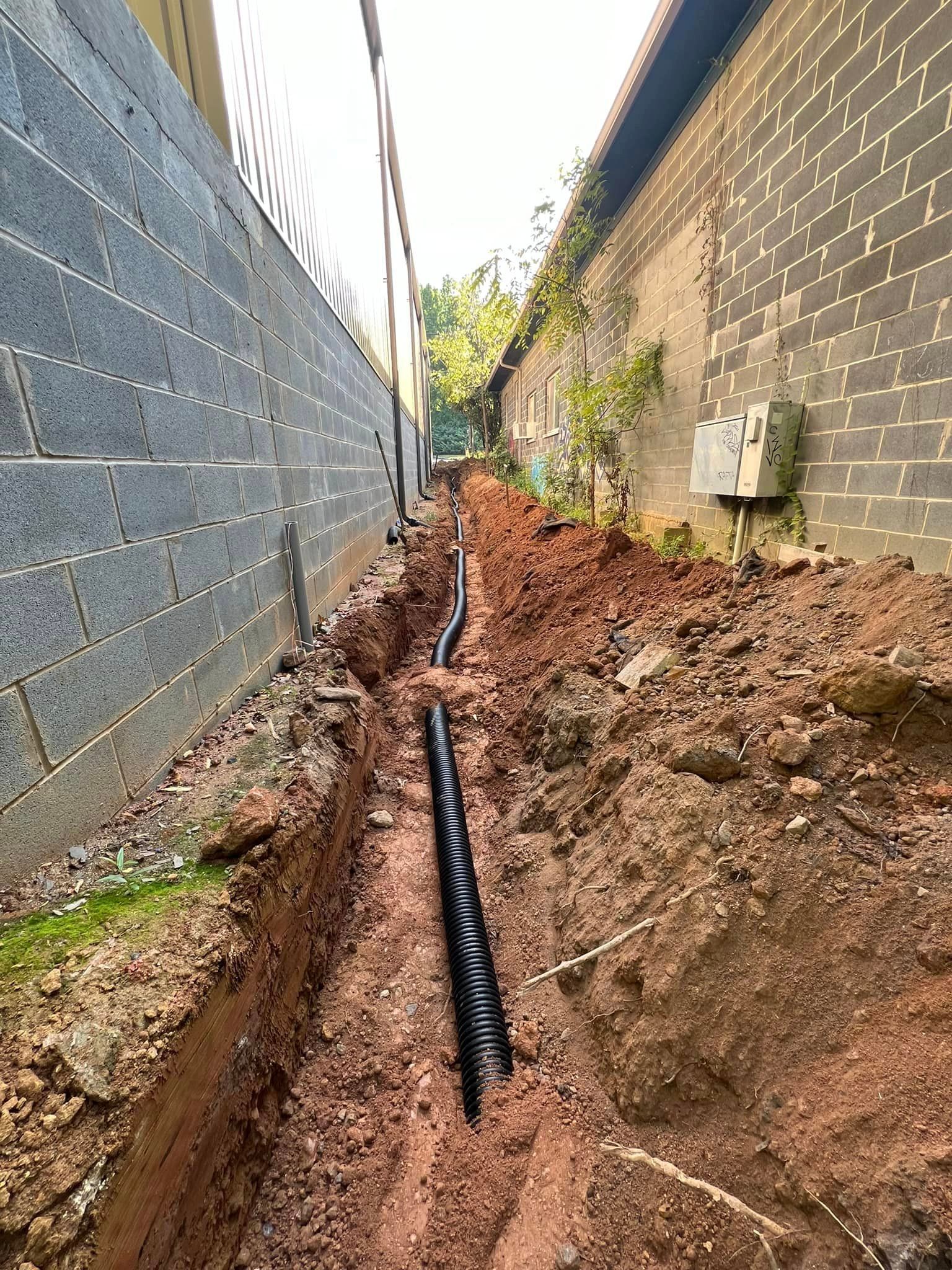 A pipe is being installed in the dirt next to a brick wall.