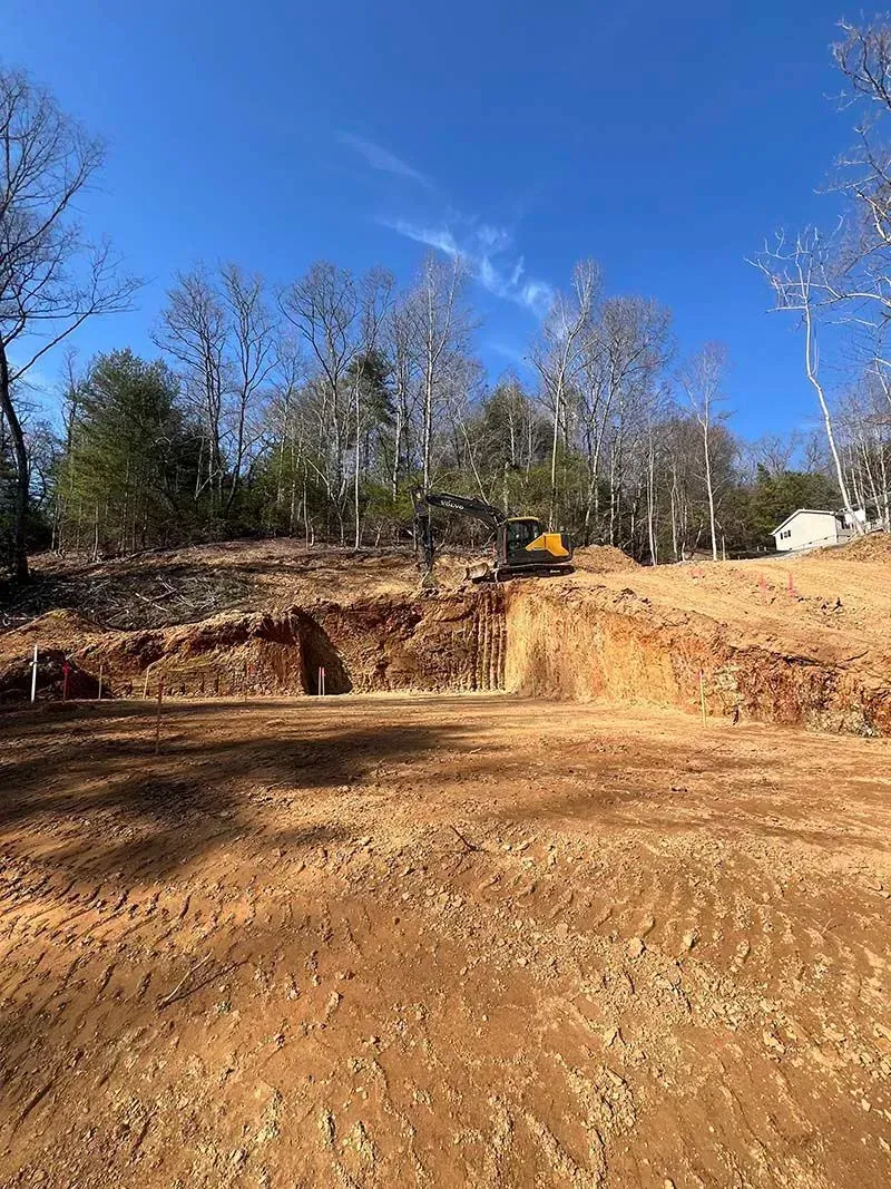 A large dirt field with trees in the background and a bulldozer in the foreground.