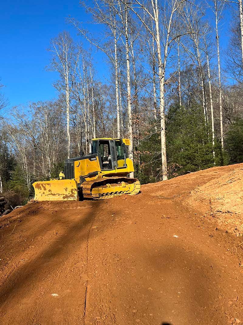 A bulldozer is driving down a dirt road in the woods.
