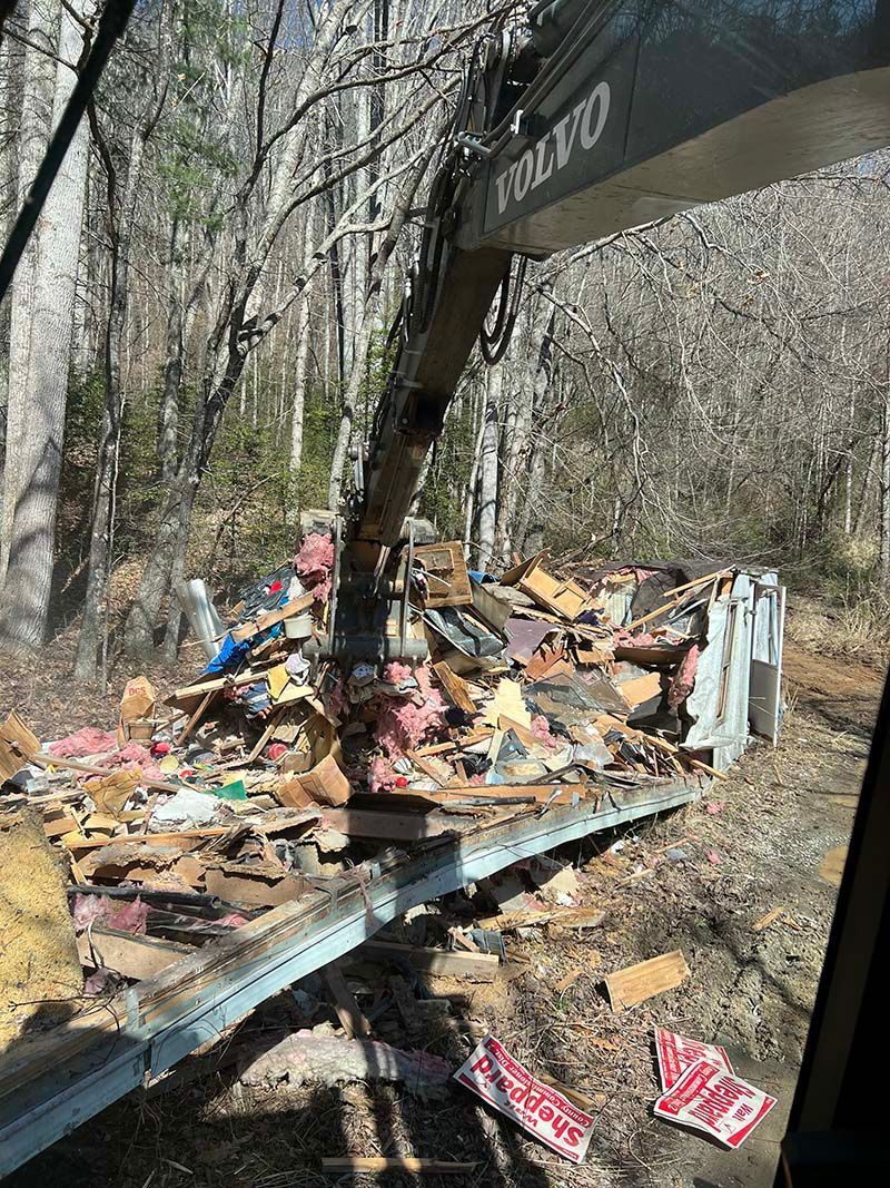 A crane is lifting a pile of wood in the woods.