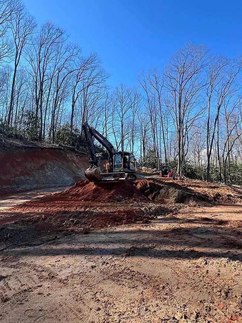 A bulldozer is digging a hole in the dirt in the middle of a forest.