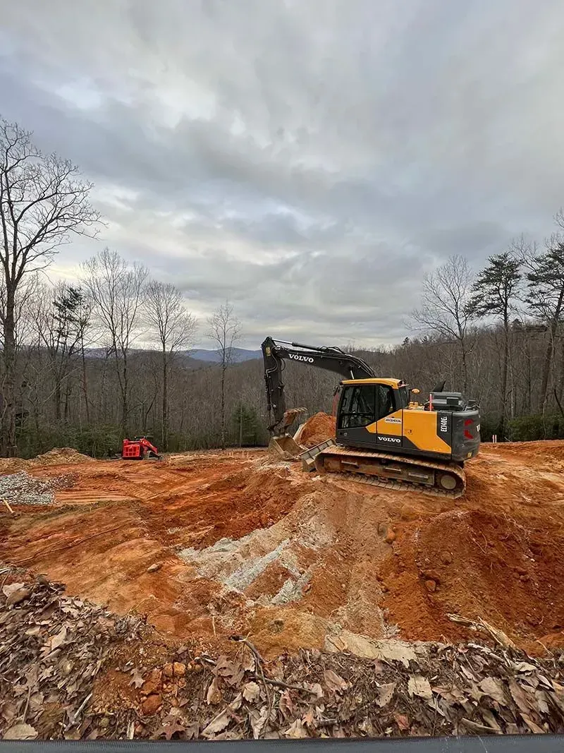 A yellow and black excavator is moving dirt in a dirt field.
