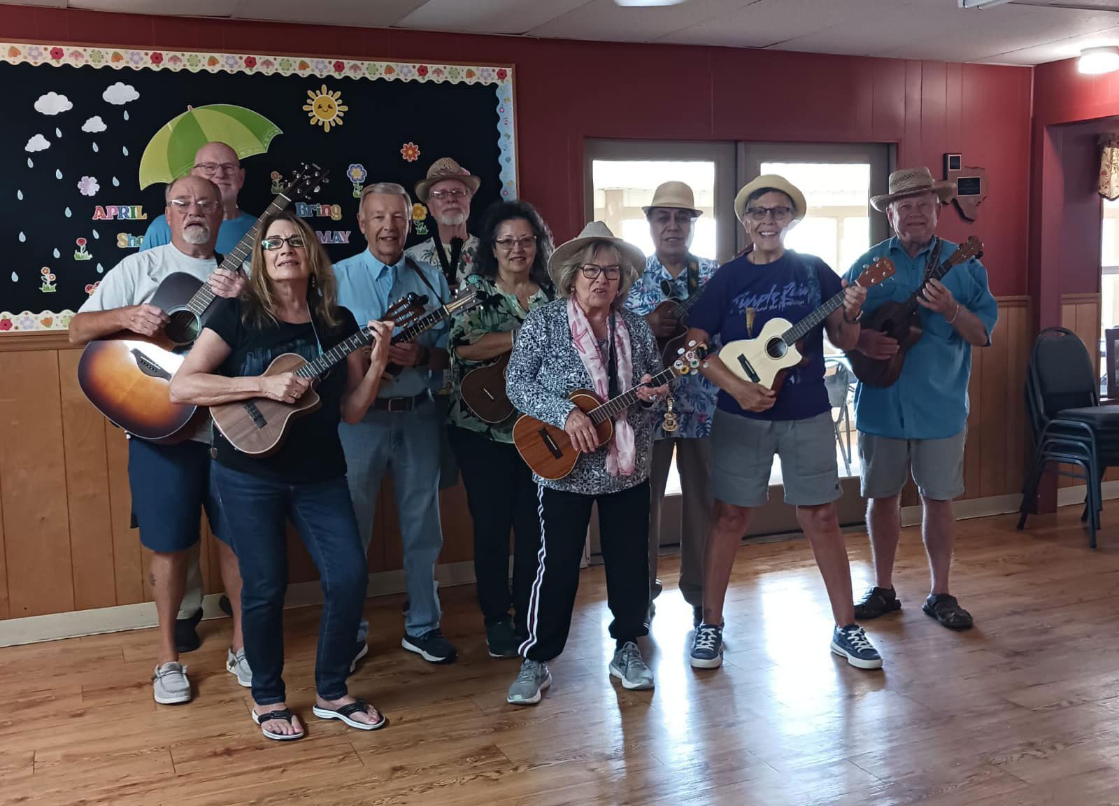 Group of musicians posing indoors with guitars and ukuleles in a wood-paneled room