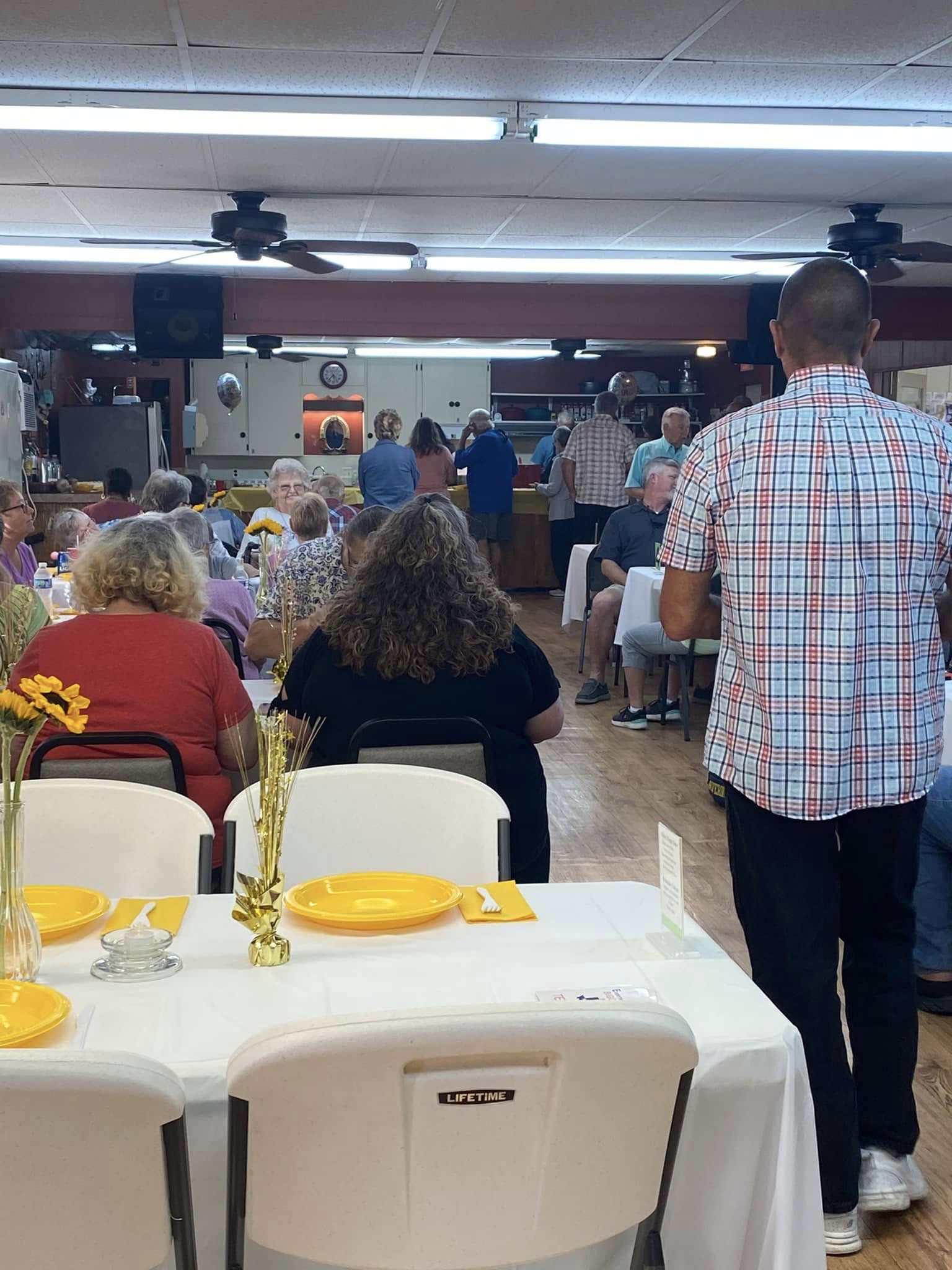 Banquet hall with seated guests at tables, facing a stage at the front.