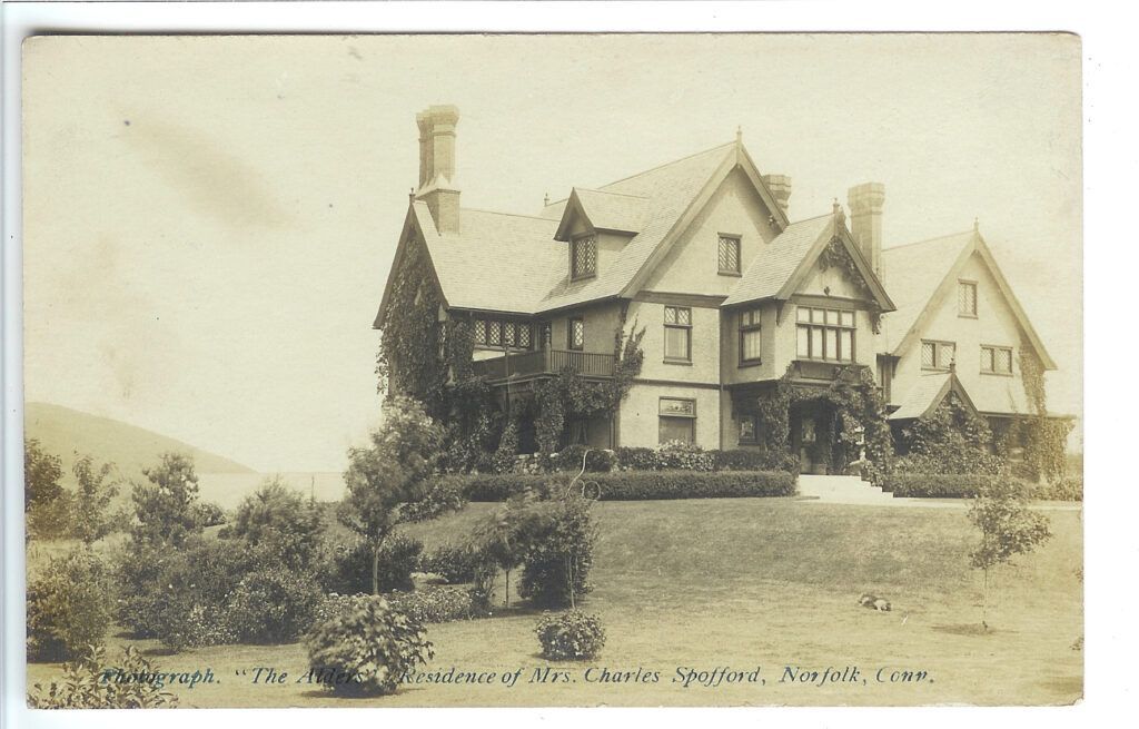 A black and white photo of a large Tudor-style Gilded-age mansion with a few trees in front of it.
