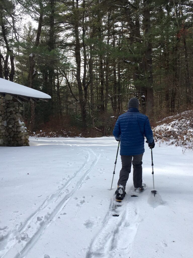 A man is snowshoeing down a snowy path in the woods.