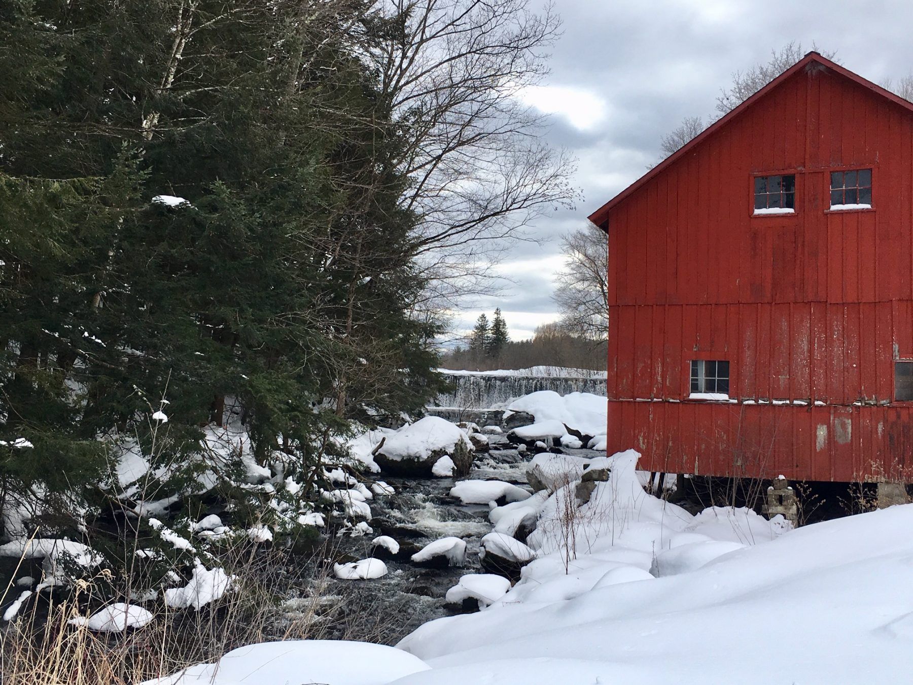 A red barn is surrounded by snow and trees