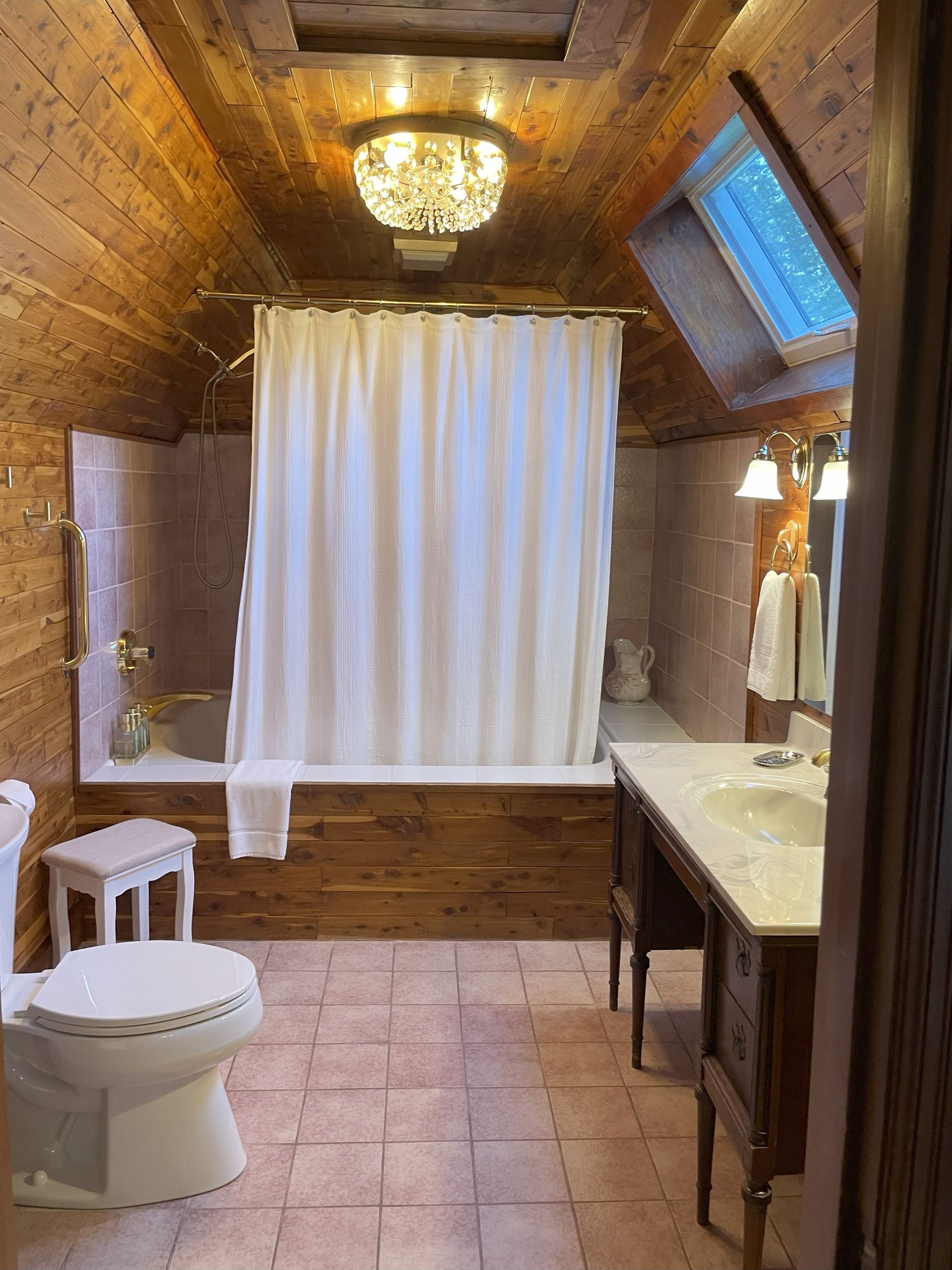 Bathroom with warm wooden panels and ceiling. Bathtub behind a curtain, toilet, vanity with a sink.