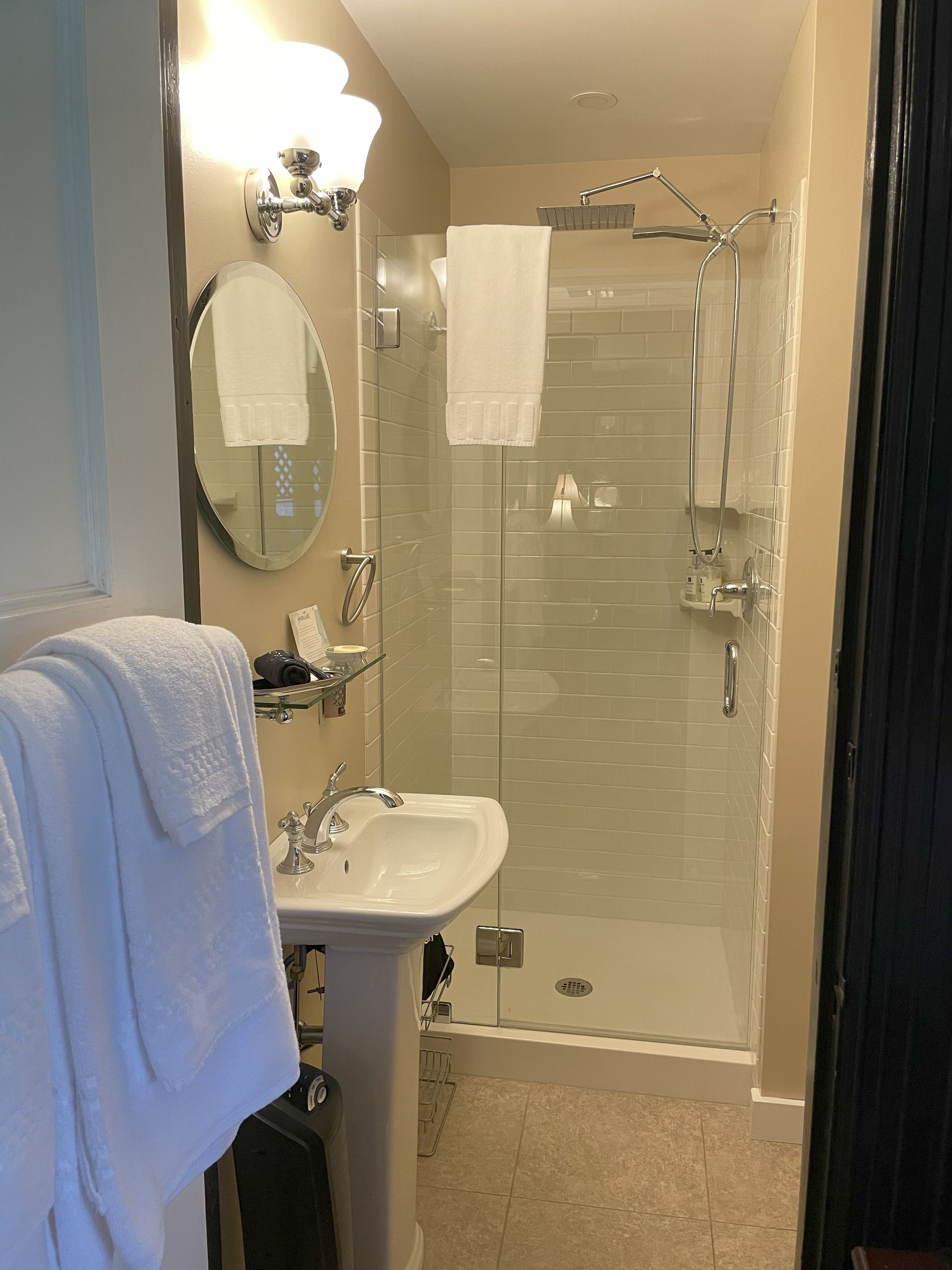 Bathroom with shower, pedestal sink, and towel rack; beige walls and flooring, white towels.