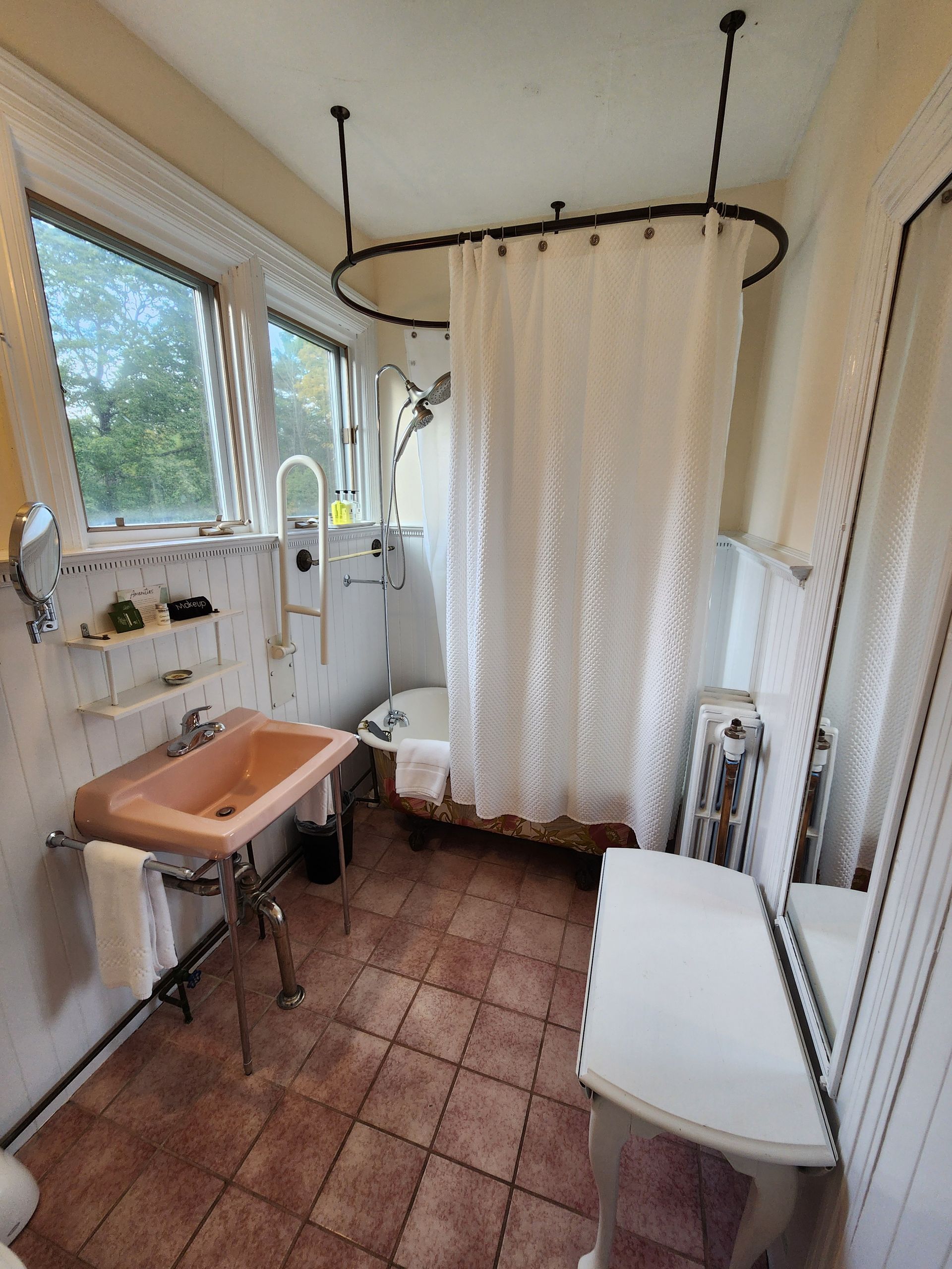 Small bathroom with pink sink, shower curtain, and oval shower rod.