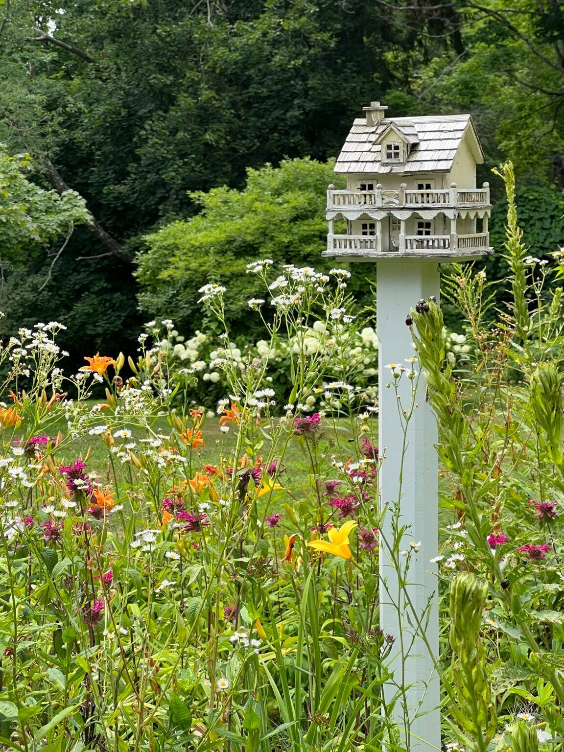 An ornate white birdhouse is sitting on top of a white pole in an English Garden.