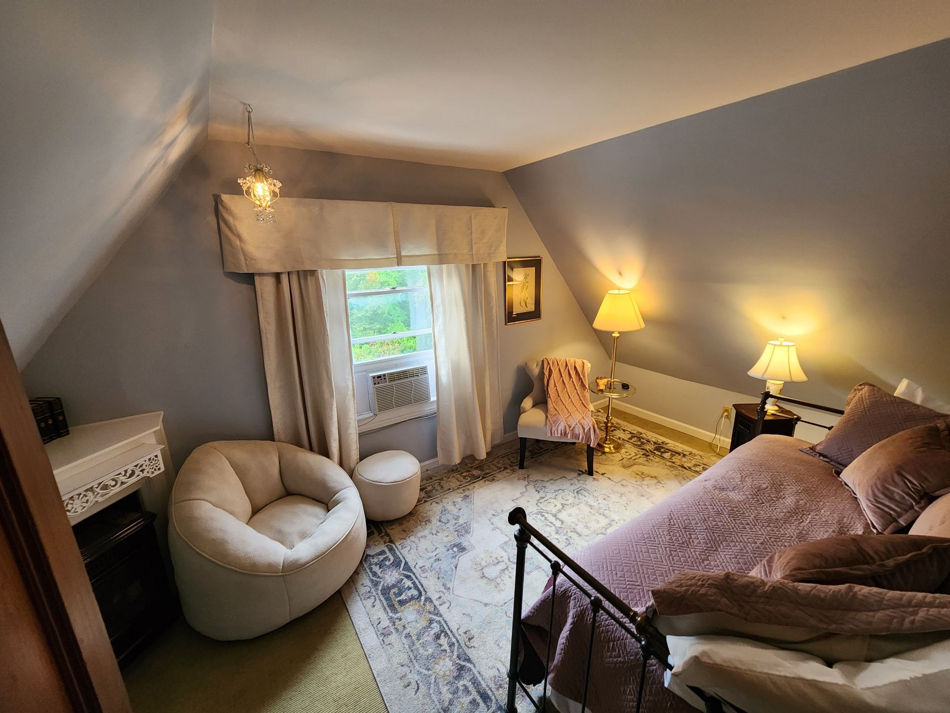Bedroom with bed, chair, and window. Beige and rose tones with blue walls and slanted ceiling.