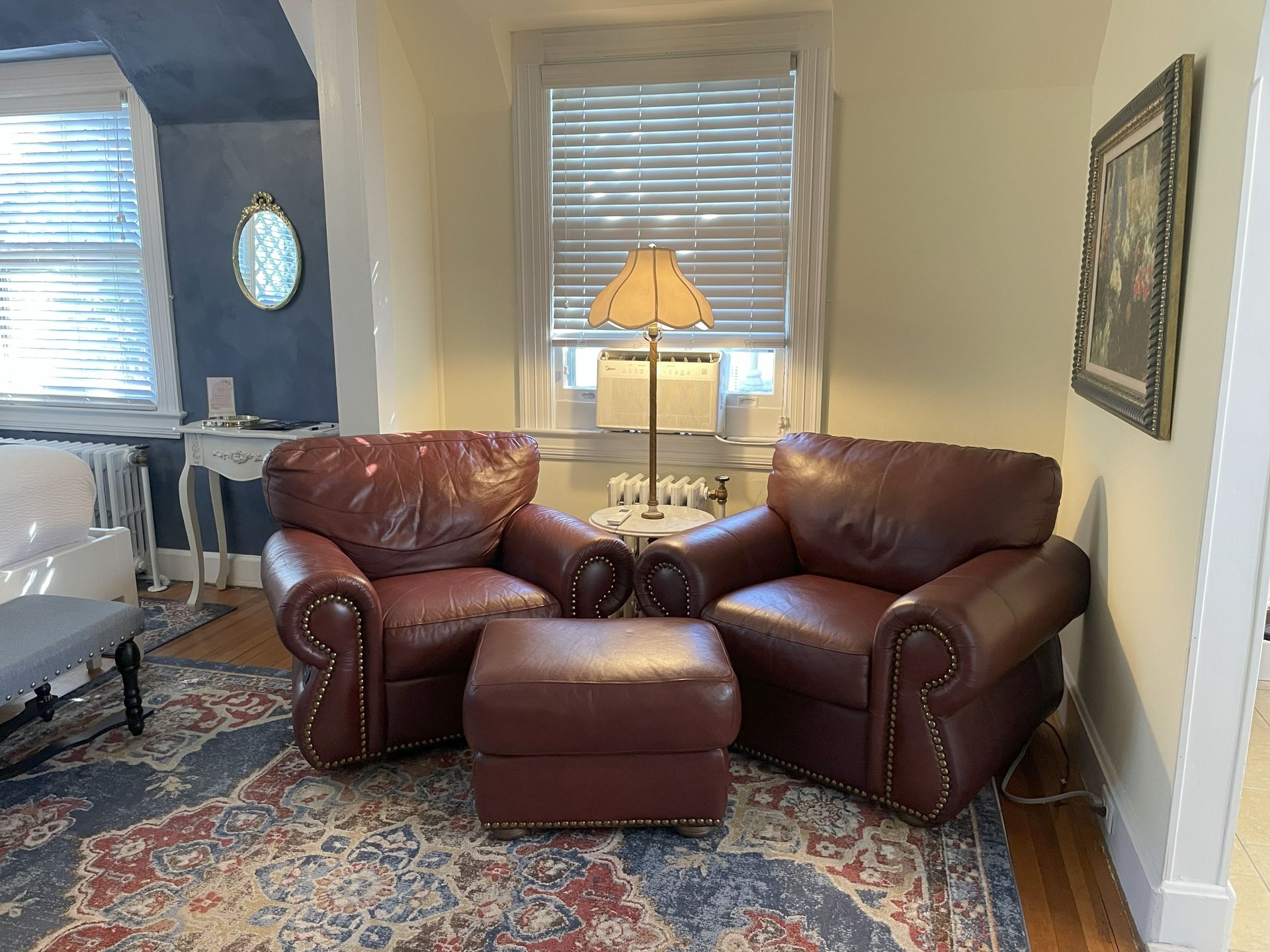 Two maroon leather armchairs with ottoman on a patterned rug, next to a window.