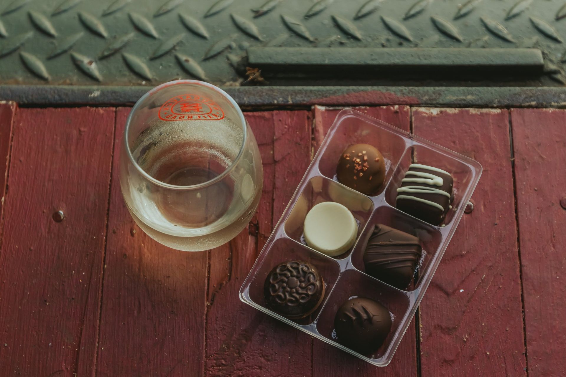 A tray of chocolates next to a glass of wine on a wooden table.