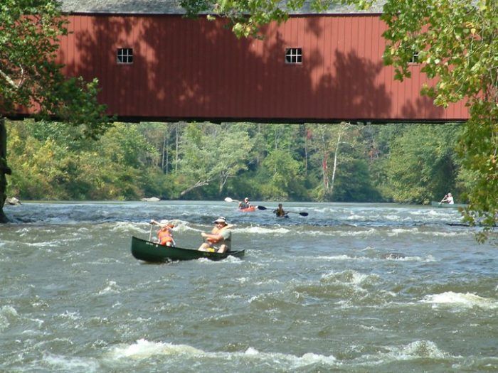 A man in a green canoe is paddling under a covered bridge