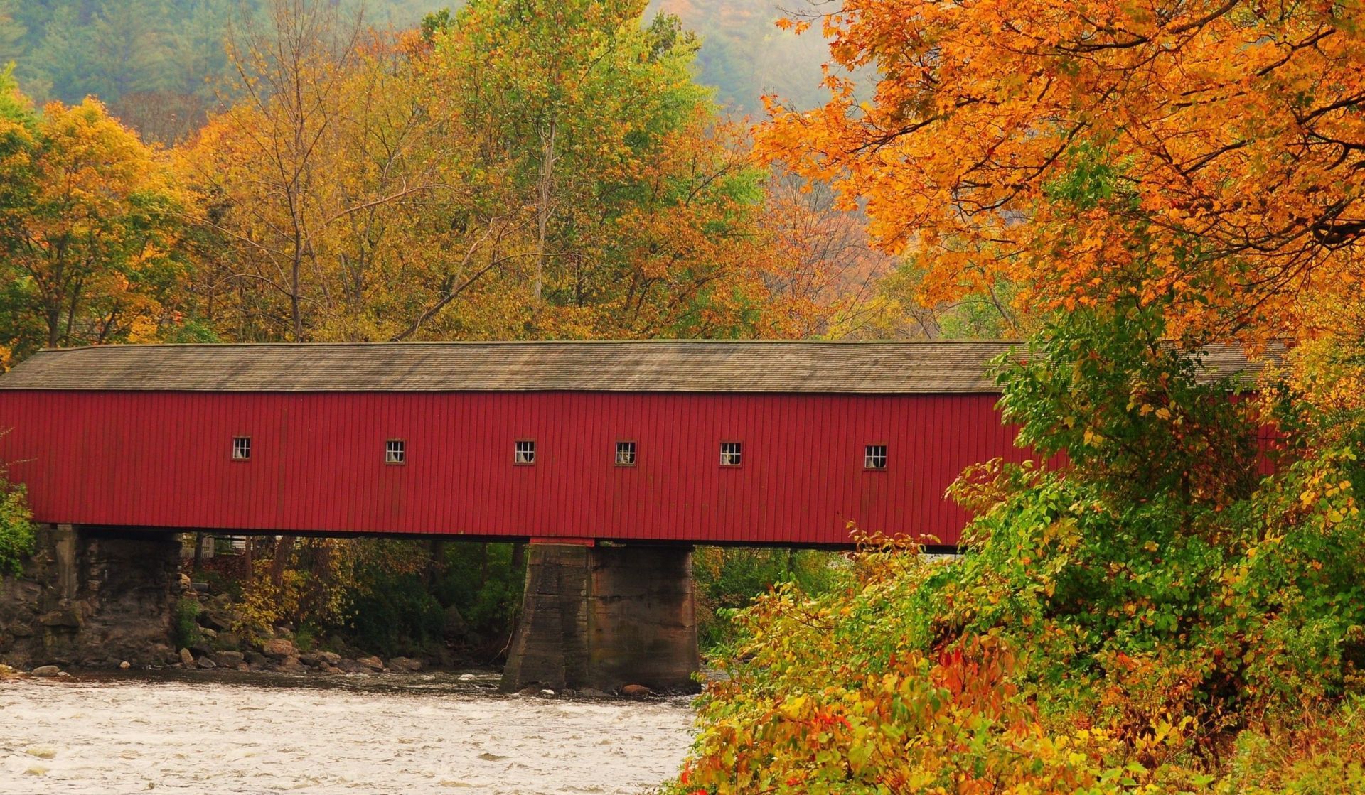 A red covered bridge over a river in autumn