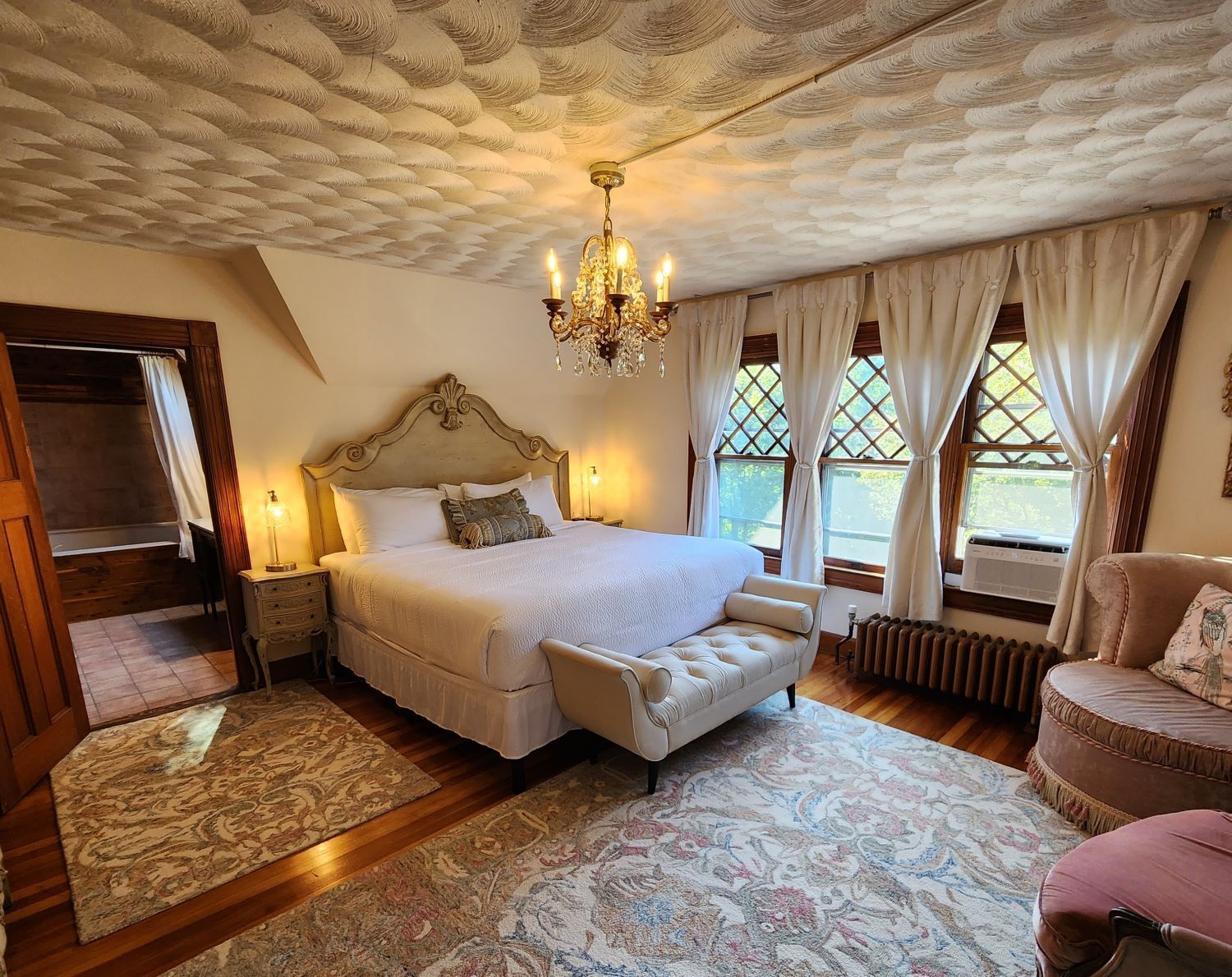 A Country French bedroom with a large bed and a vintage chandelier at a Victorian-style New England Country Inn.