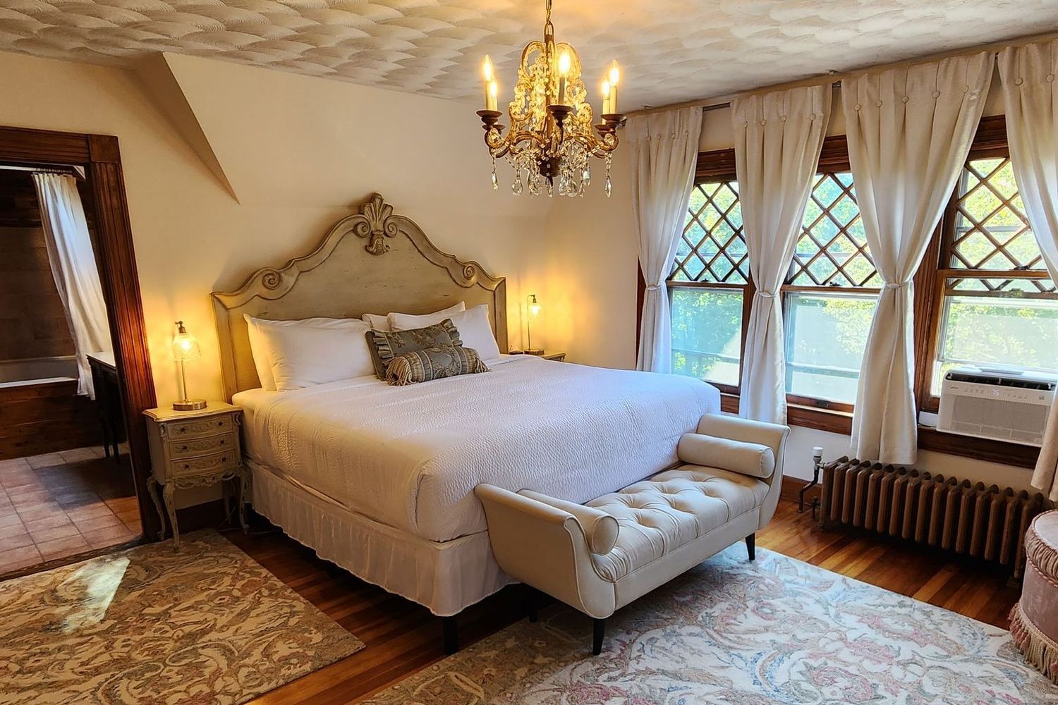 A Country French style bedroom at a New England Country Inn with a king-size bed, a bench, and a vintage chandelier.