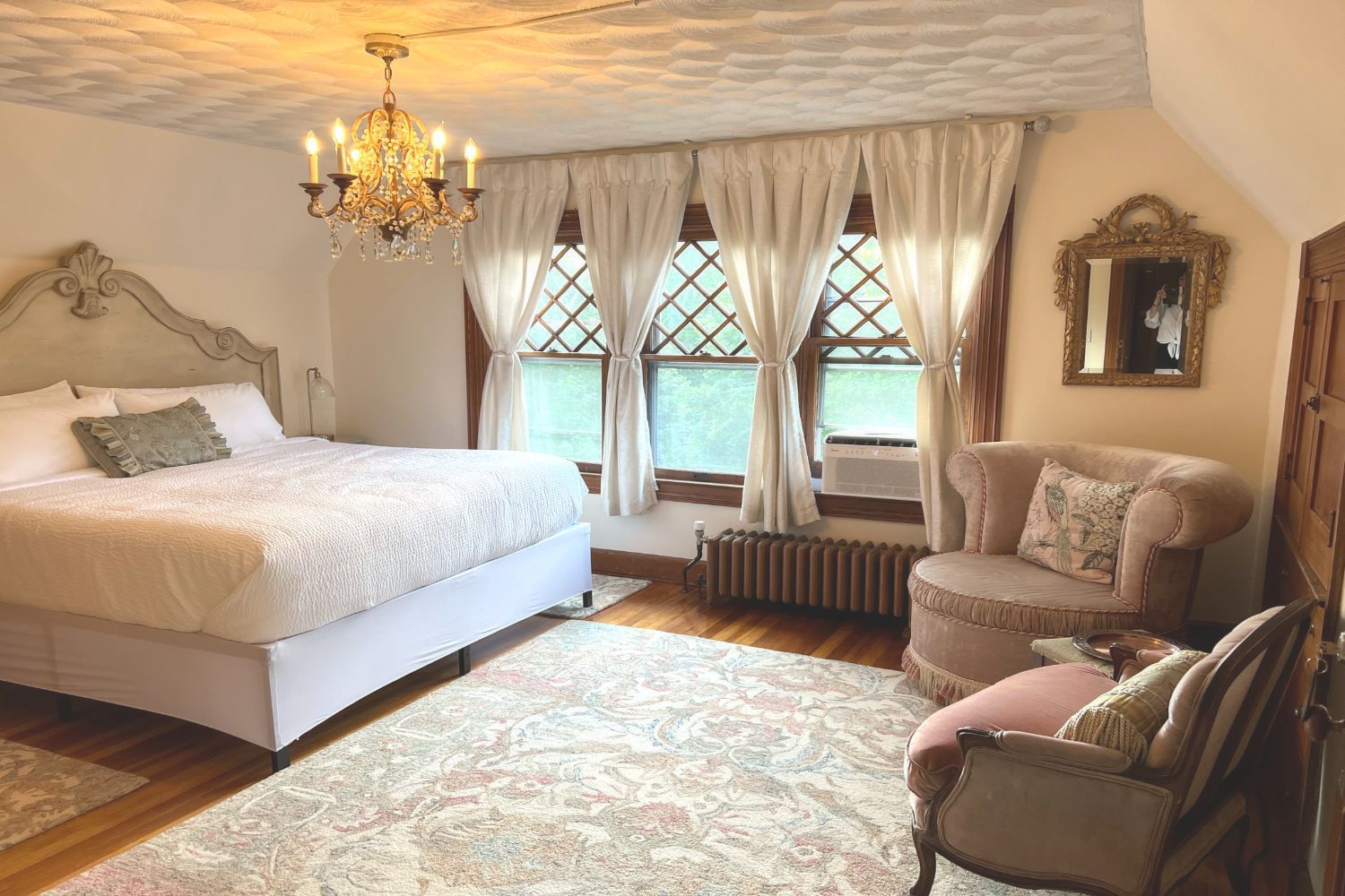 A romatic Country French bedroom at a New England Country Inn with a large bed, chair, diaomond-paned windows, and chandelier.