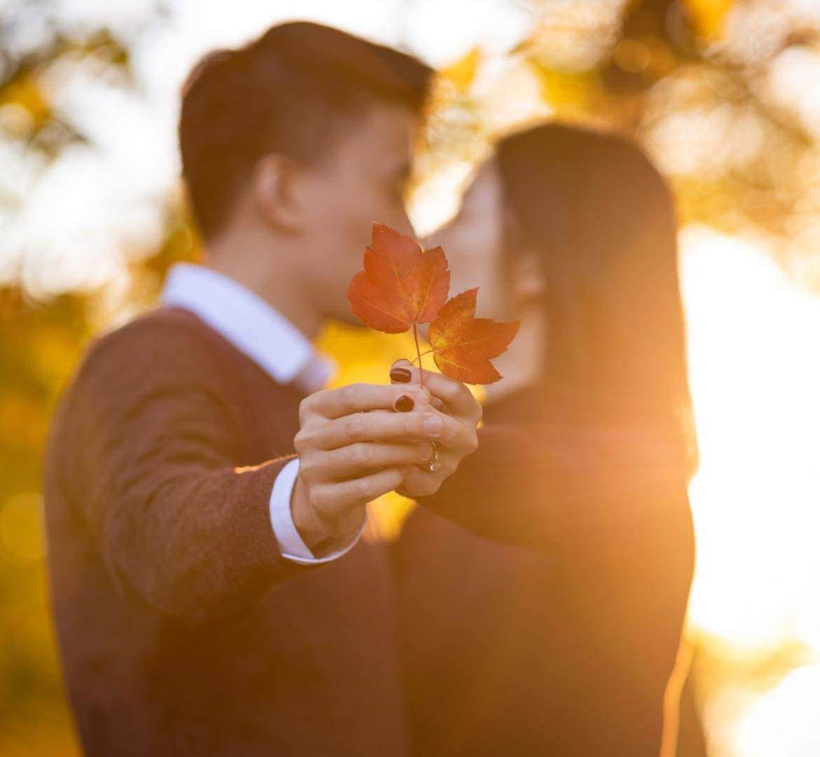 A man is holding a leaf in front of a woman who is kissing him.