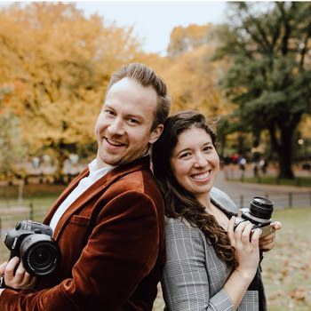 A man and a woman are standing back to back holding cameras.