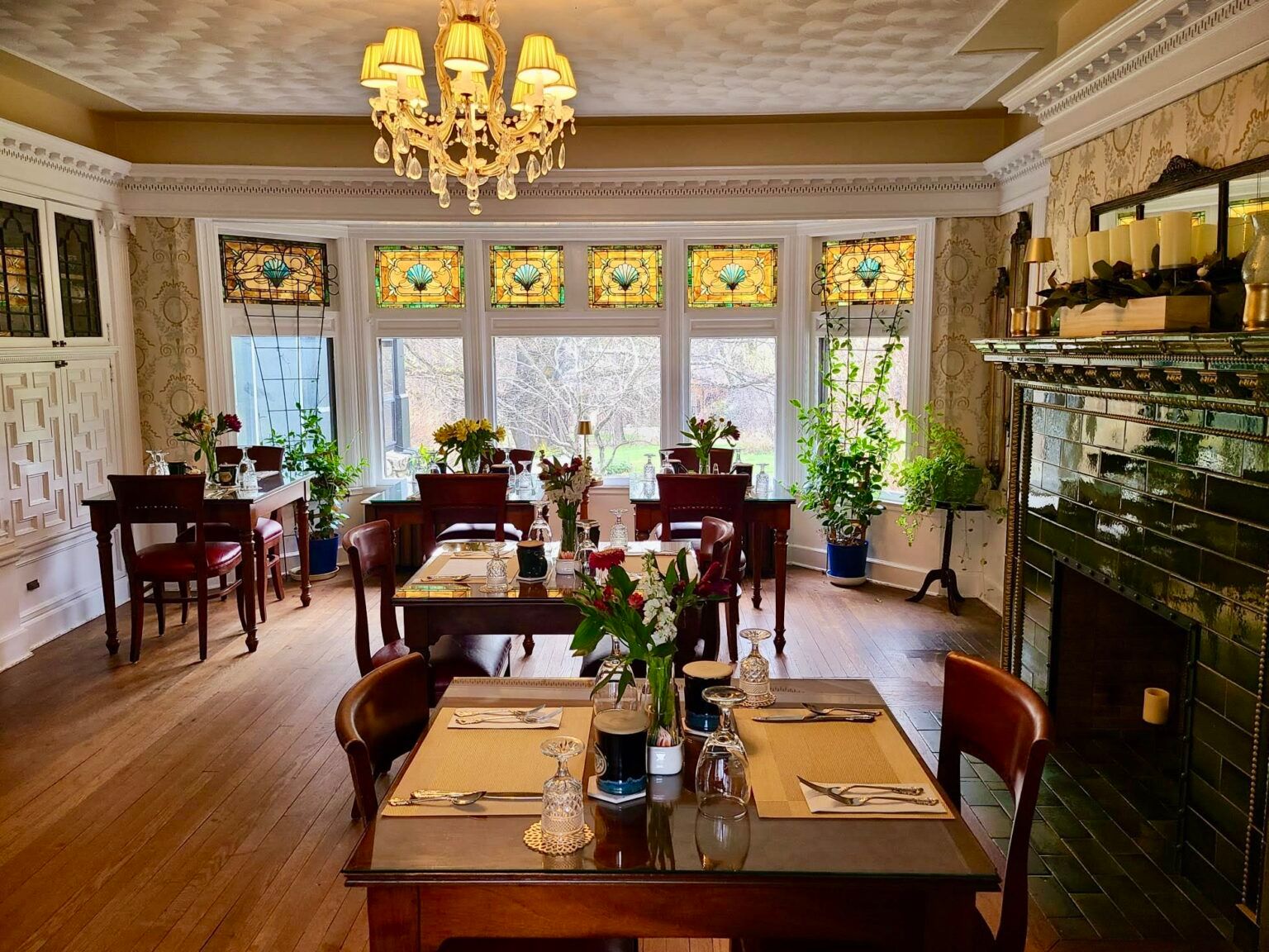 A romantic restaurant dining room with stained glass windows, a chandelier, and a fireplace.