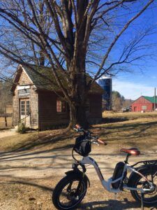 An electric bike is parked under a tree in front of a house.