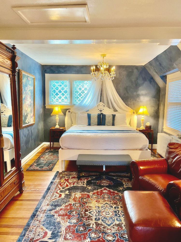 A romantic bedroom at a New England Country Inn with a bed, a bench, a rug, and a crystal chandelier.