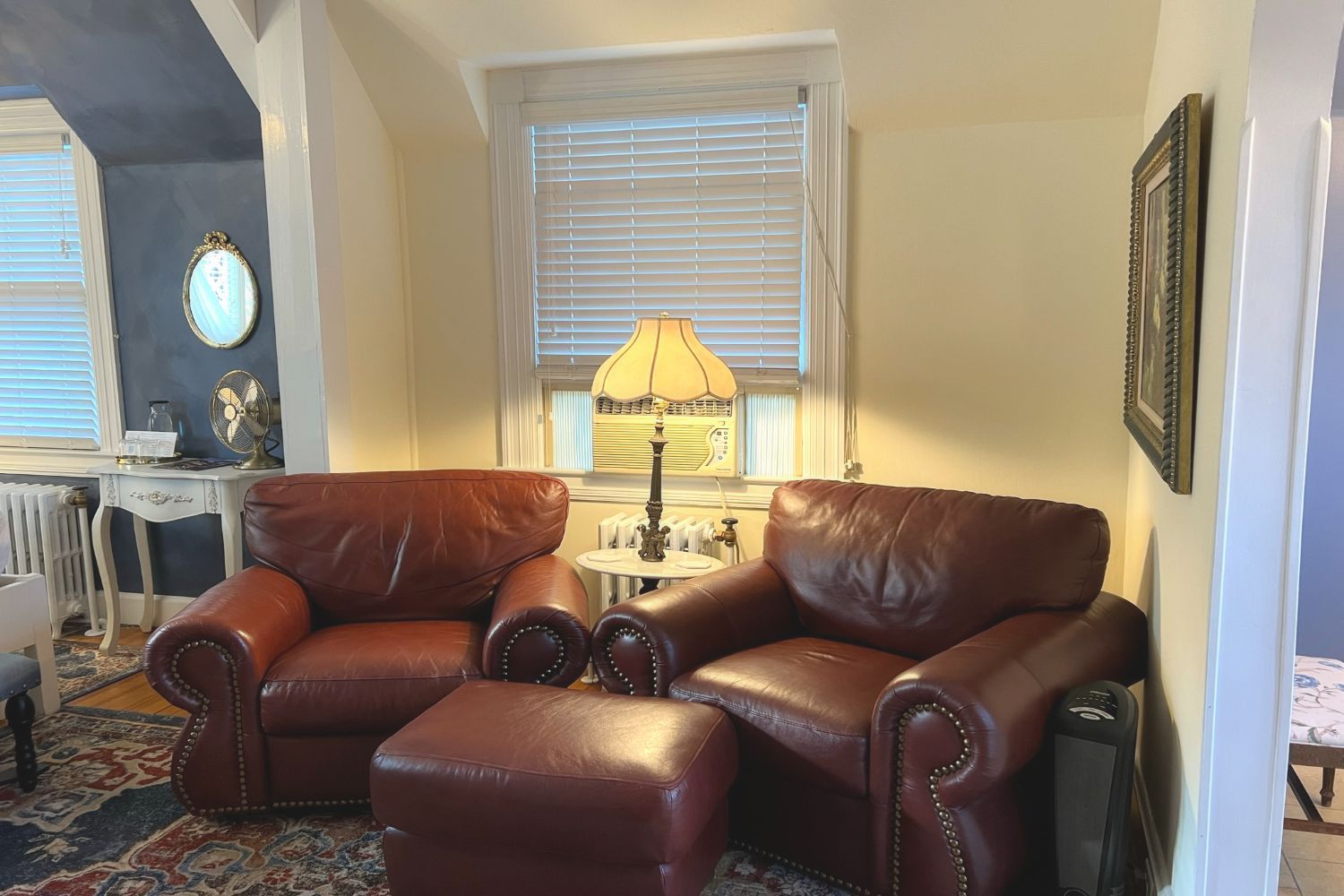 A sitting area at a New England Country Inn with two red leather chairs, vintage lamp, and an ottoman