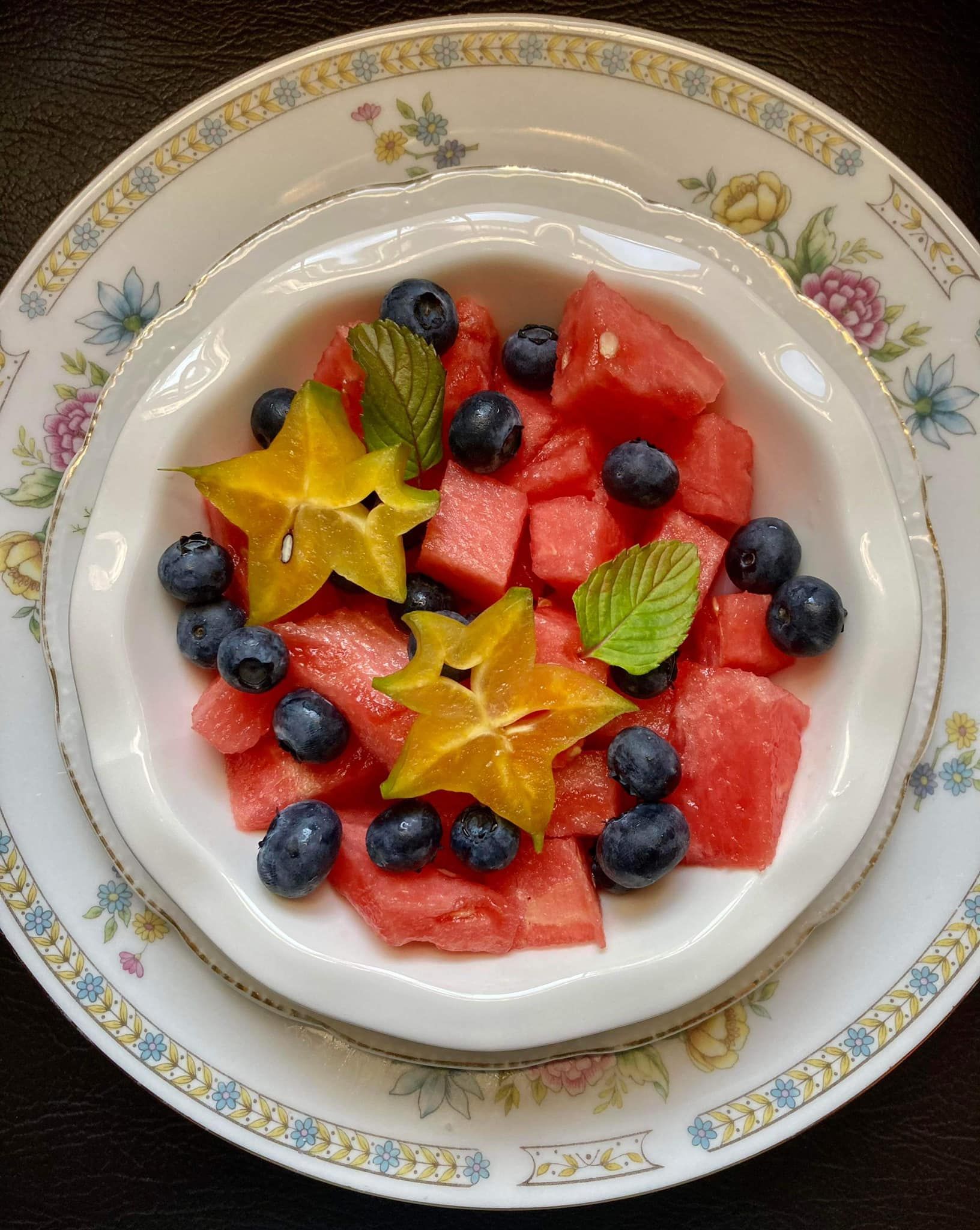 Watermelon, blueberries, and starfruit salad in a white bowl on a floral-patterned plate.