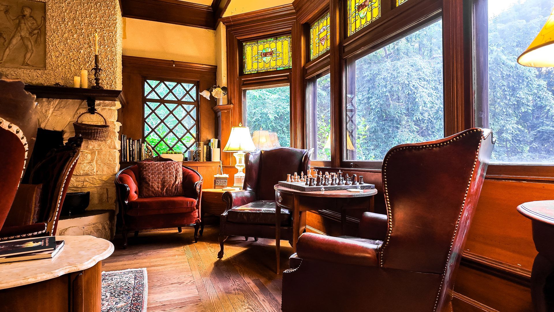 Cozy Great Room with leather armchairs, chess table, and bay window.  Warm lighting illuminates the wooden interior.