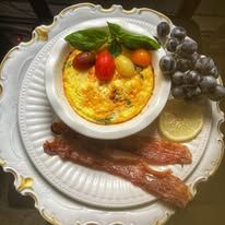 There is a bowl of food on a plate with bacon and grapes.