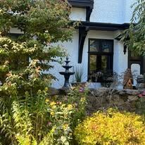 A white house with a fountain in front of it surrounded by trees and bushes.