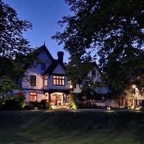 A large house is lit up at night surrounded by trees.