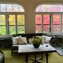 A living room with a couch , table , vase of flowers and a glass of wine.